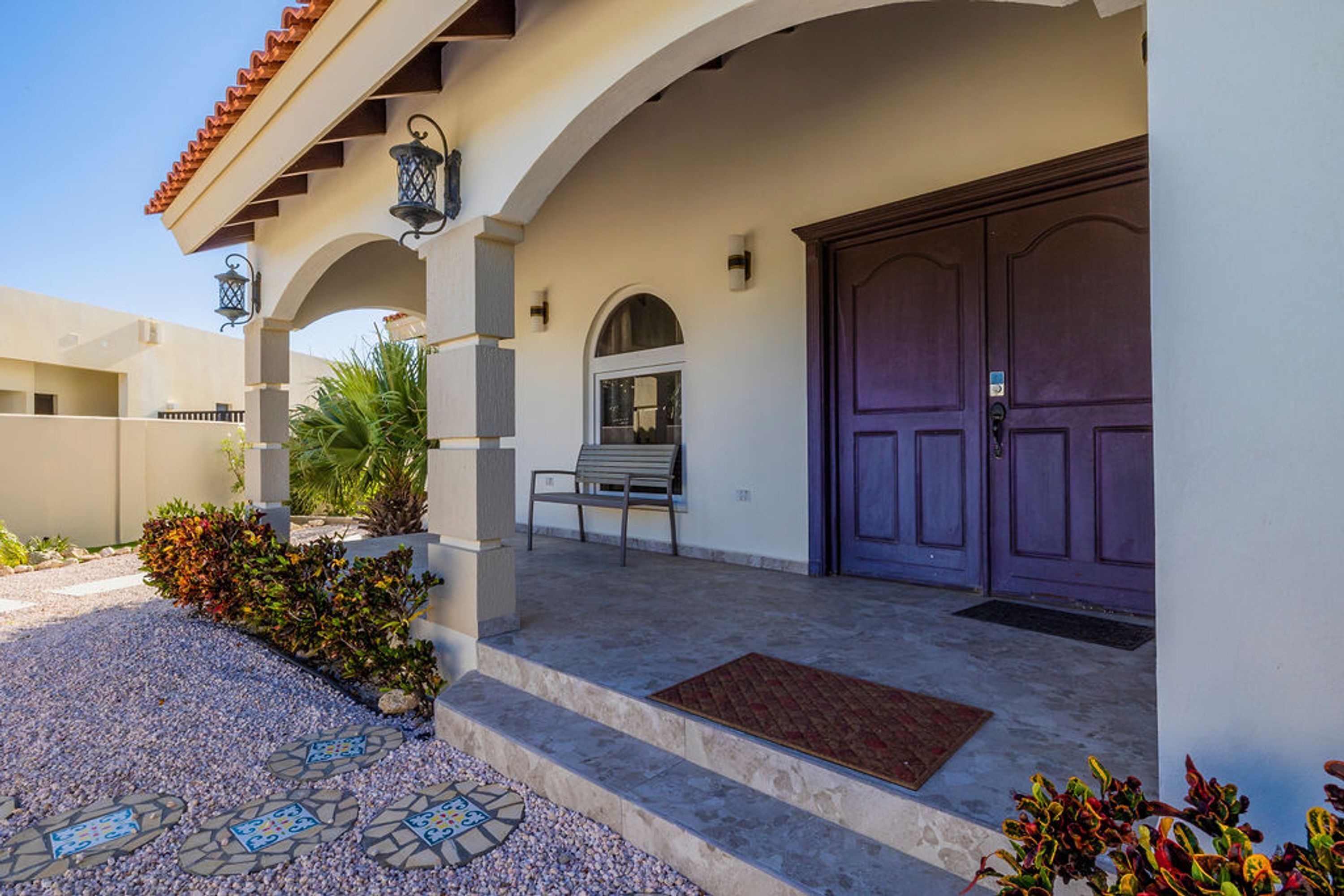 A building with a tiled entrance, a bench, and a purple door.