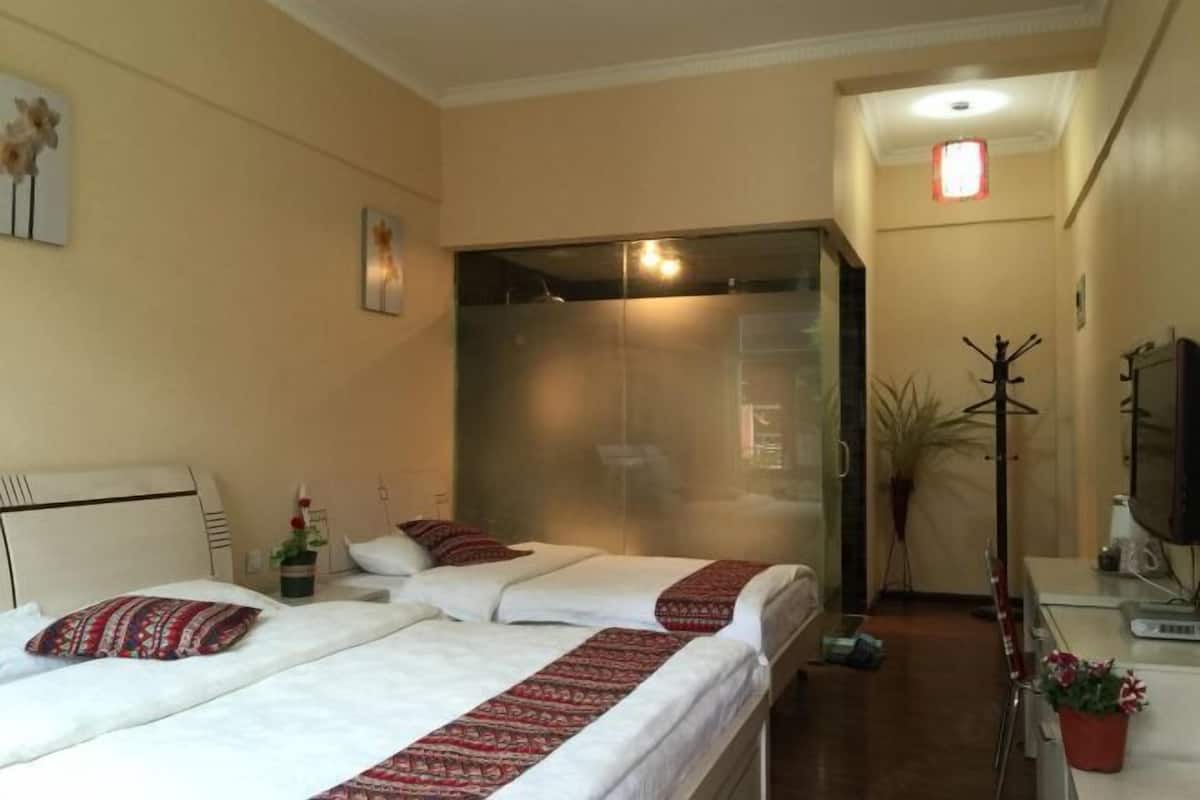 A hotel room with two beds, a coat rack, a television, and a potted plant.