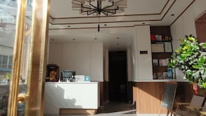 A hotel reception area with a modern chandelier, a reception desk, a plant, and a chalkboard sign. - Shangri-la Xiangruiju Inn (Shangri-La)