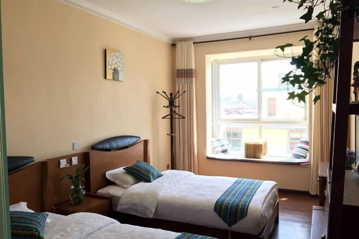 A hotel room with two beds, a window with a view, a coat rack, and a plant.