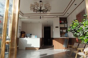Un hall de hotel con una recepción, un candelabro grande y un área de descanso con sillas.