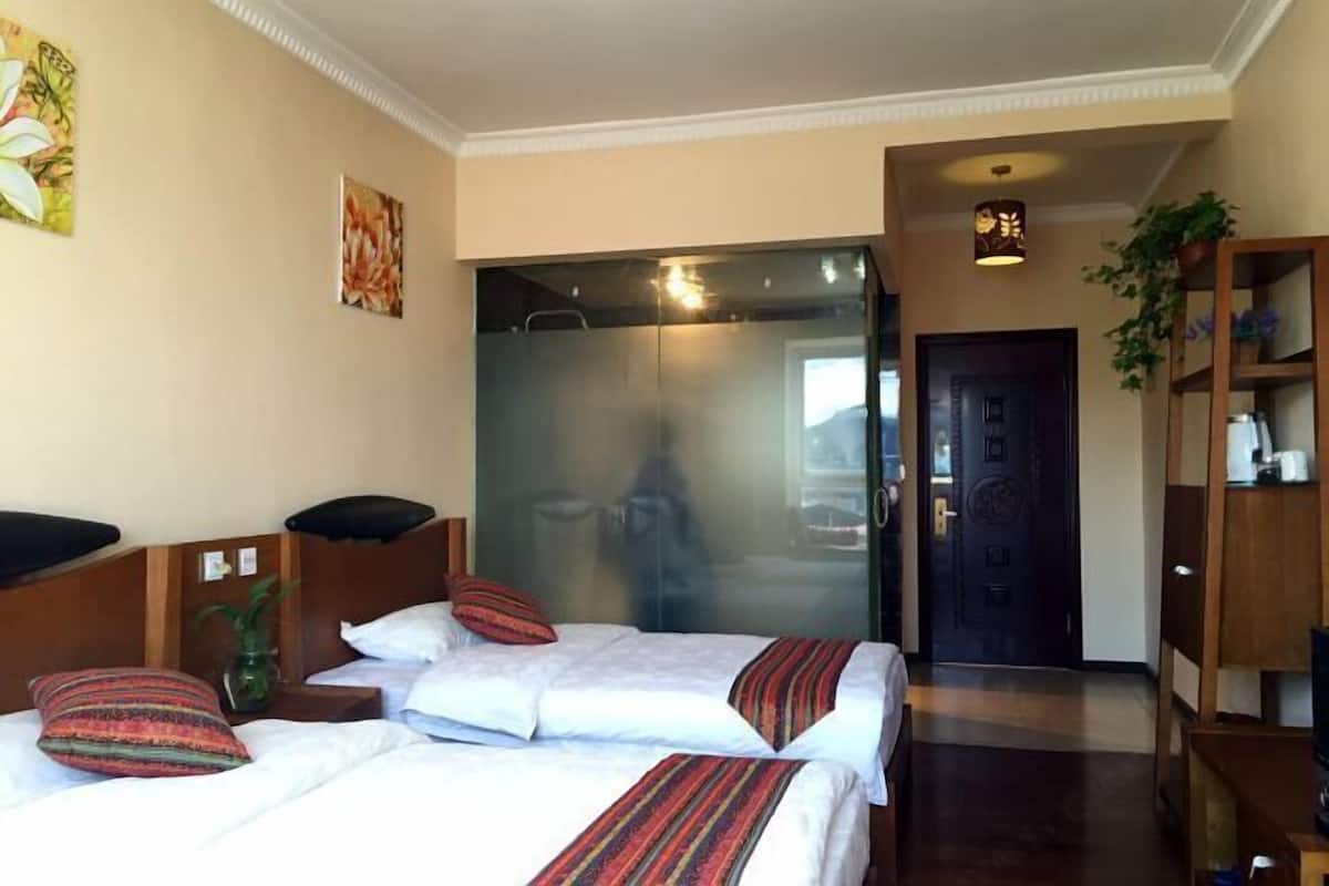 A hotel room with two beds, a wooden headboard, a mirror, a potted plant, and a door leading to another room.
