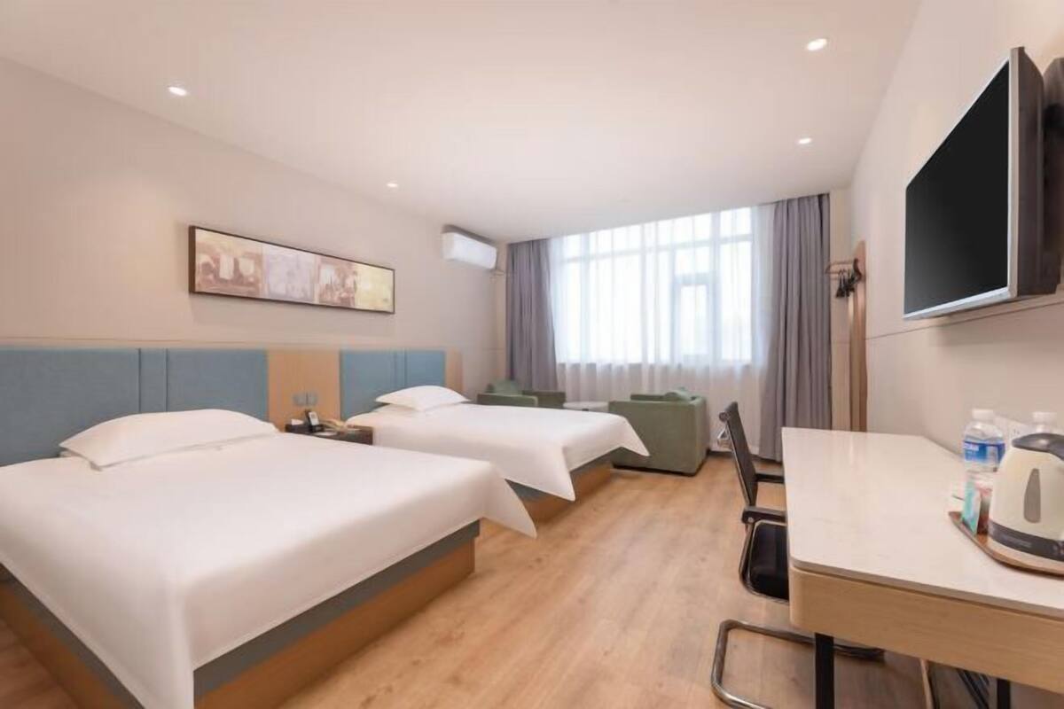 Ein Hotelzimmer mit zwei Betten, einem Schreibtisch, einem Fernseher und einem Vorhangfenster.