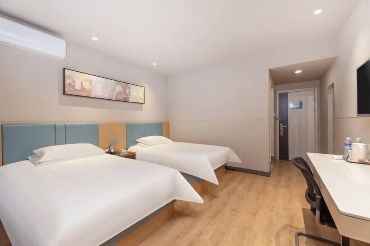 Ein Hotelzimmer mit zwei Betten, einem Schreibtisch, einem Stuhl, einem Bild an der Wand und einer Tür zu einem weiteren Raum.