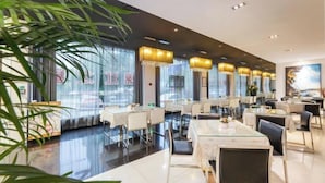 Ein modernes Restaurant mit Glastischen, weißen Stühlen und großen Fenstern.