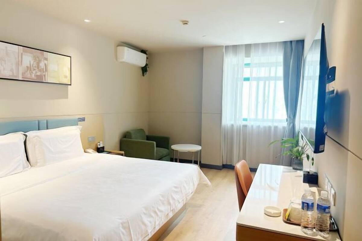 Ein Hotelzimmer mit Bett, Schreibtisch, Stuhl, kleinem Tisch, Fernseher und einem Fenster mit Vorhängen.