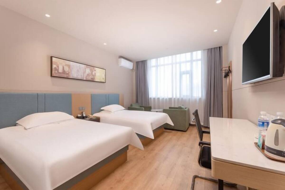 Ein Hotelzimmer mit zwei Betten, einem Schreibtisch, einem Sessel, einem Fernseher und einem Fenster mit Vorhängen.
