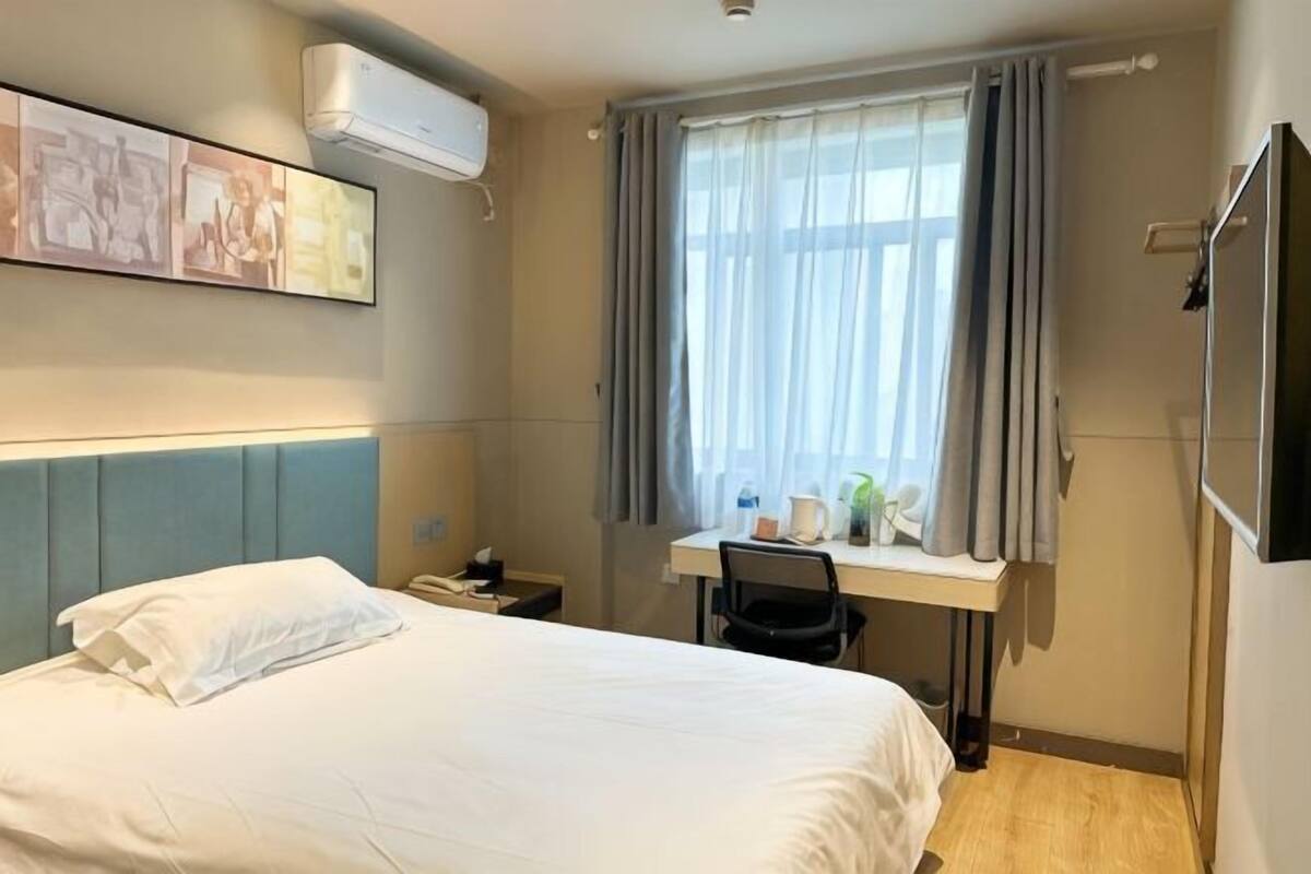 Ein Hotelzimmer mit Bett, Schreibtisch, Stuhl und einem Fenster mit Vorhängen.