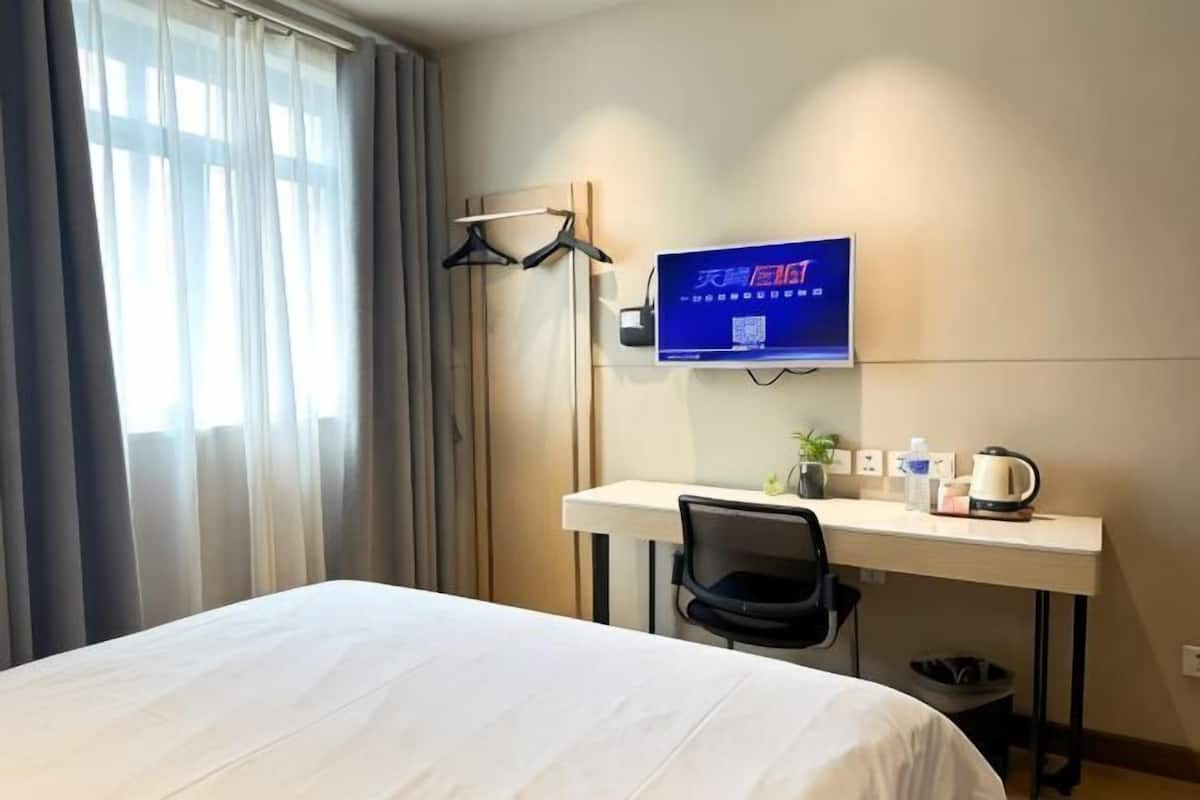 A hotel room with a bed, a desk with a chair, a television, and a window with curtains.