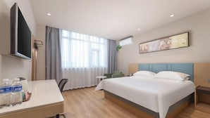 Ein Hotelzimmer mit einem Bett, einem Schreibtisch mit Wasserflaschen, einem Fernseher, einem Fenster mit Vorhängen und einem Bild an der Wand.