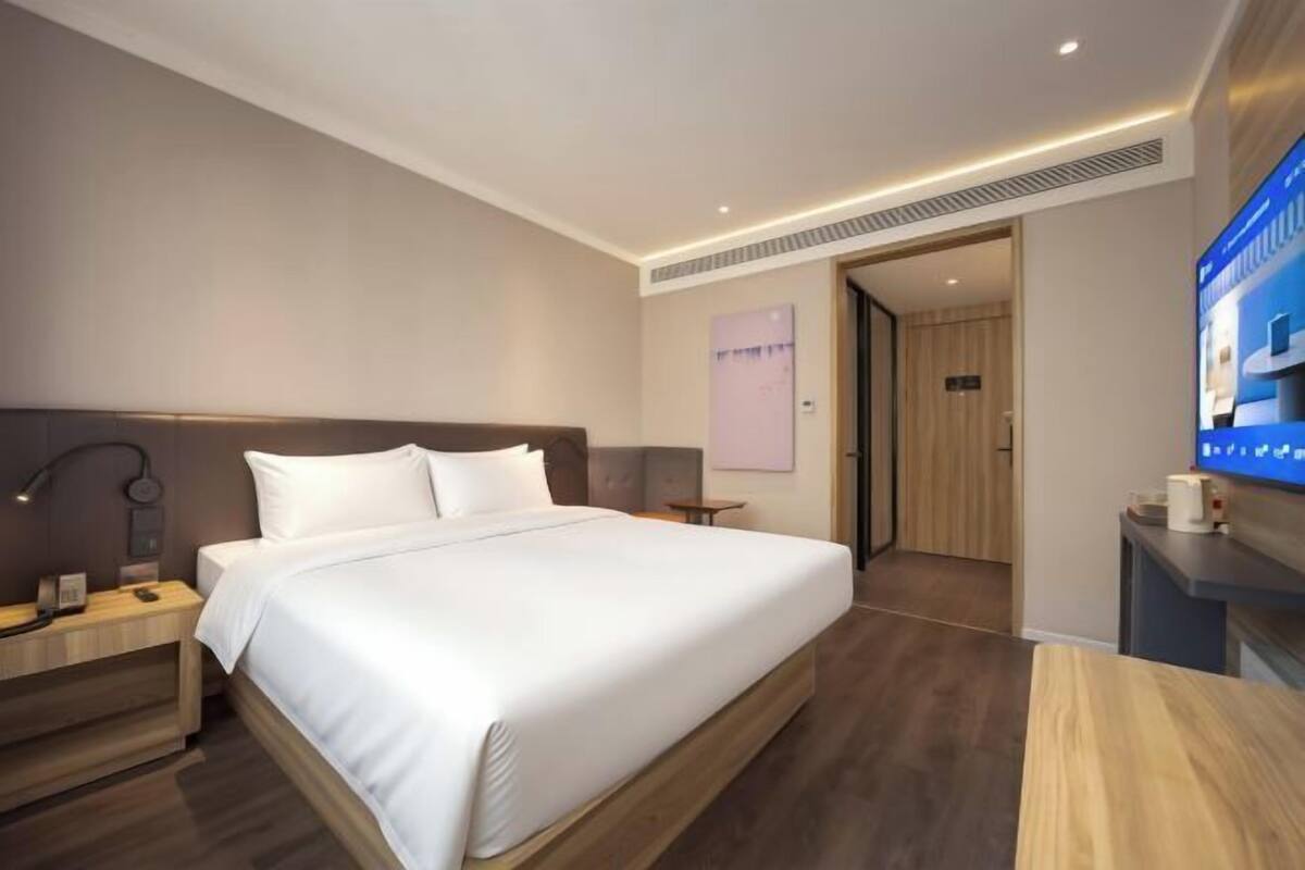 A modern hotel room with a large bed, bedside tables, a flat-screen TV, and a wooden floor.