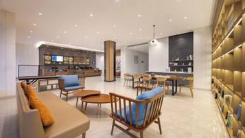 A modern hotel lobby with a bar area, seating arrangements, and a bookshelf.