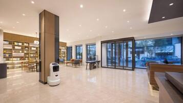 A spacious lobby with a robot, seating areas, and a large bookshelf.