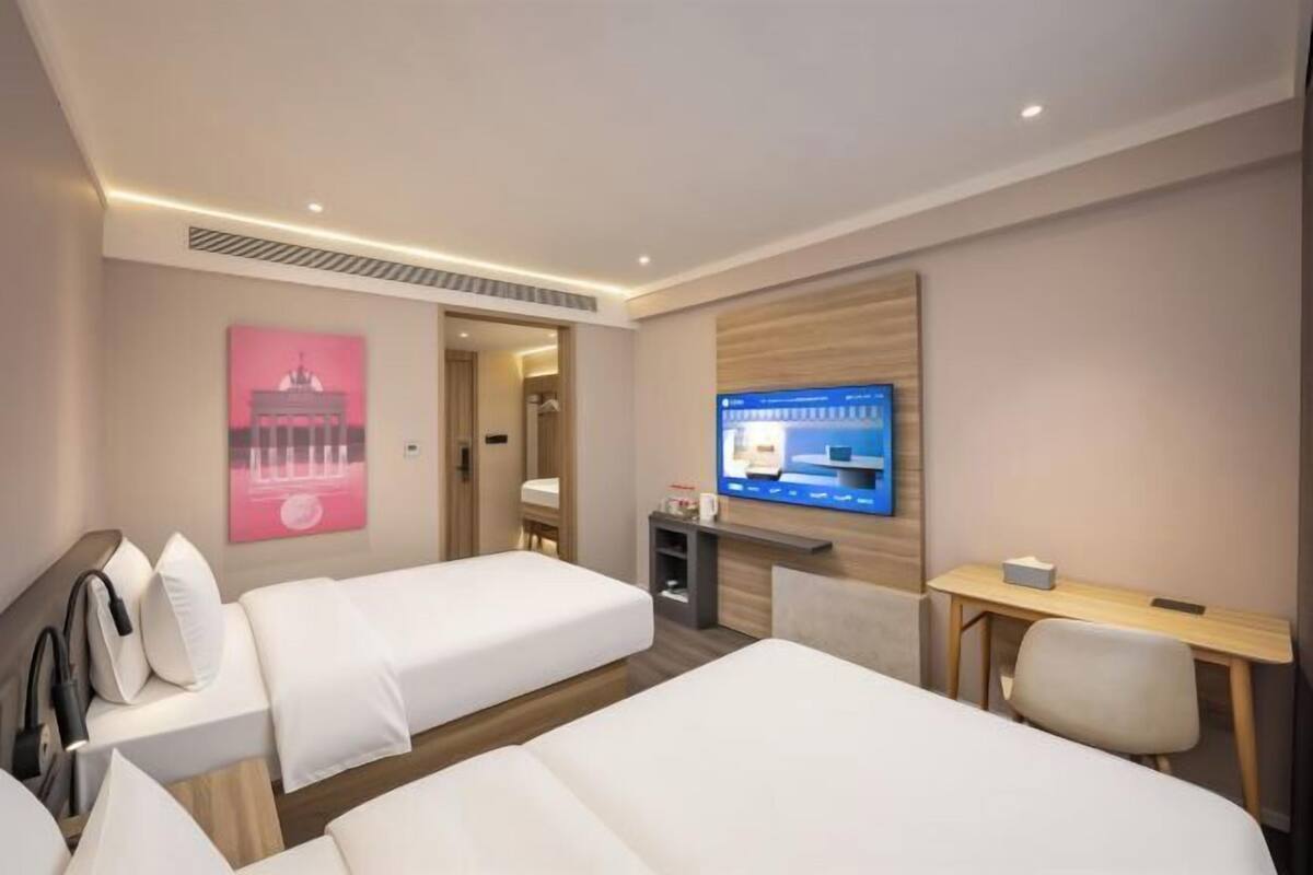 A hotel room with two beds, a desk, a TV, and a poster on the wall.