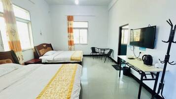 A hotel room with two beds, a desk, a chair, a television, and a coat rack.