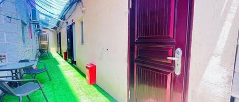 A narrow alleyway with a red door, a small table with chairs, and a trash bin.