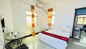 Quarto de hotel com cama, escrivaninha, cadeira e janela com cortinas.