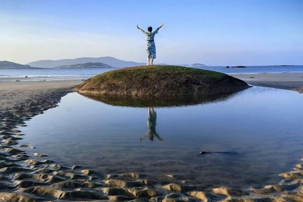 A person standing on a small island with arms raised, surrounded by calm water and a clear sky. - Shiqiu Homestay, Island Island, Pingtan Island (Pingtan County)
