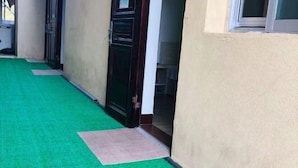 Um corredor com carpete verde que leva a uma porta, um tapete pequeno na entrada e uma parede bege.