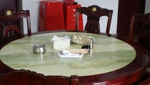 Mesa de jantar redonda com tampo de mármore, rodeada por cadeiras de madeira com detalhes entalhados.