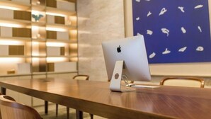 Une salle de conférence avec une table en bois, un ordinateur Apple iMac et une œuvre d’art encadrée accrochée au mur.