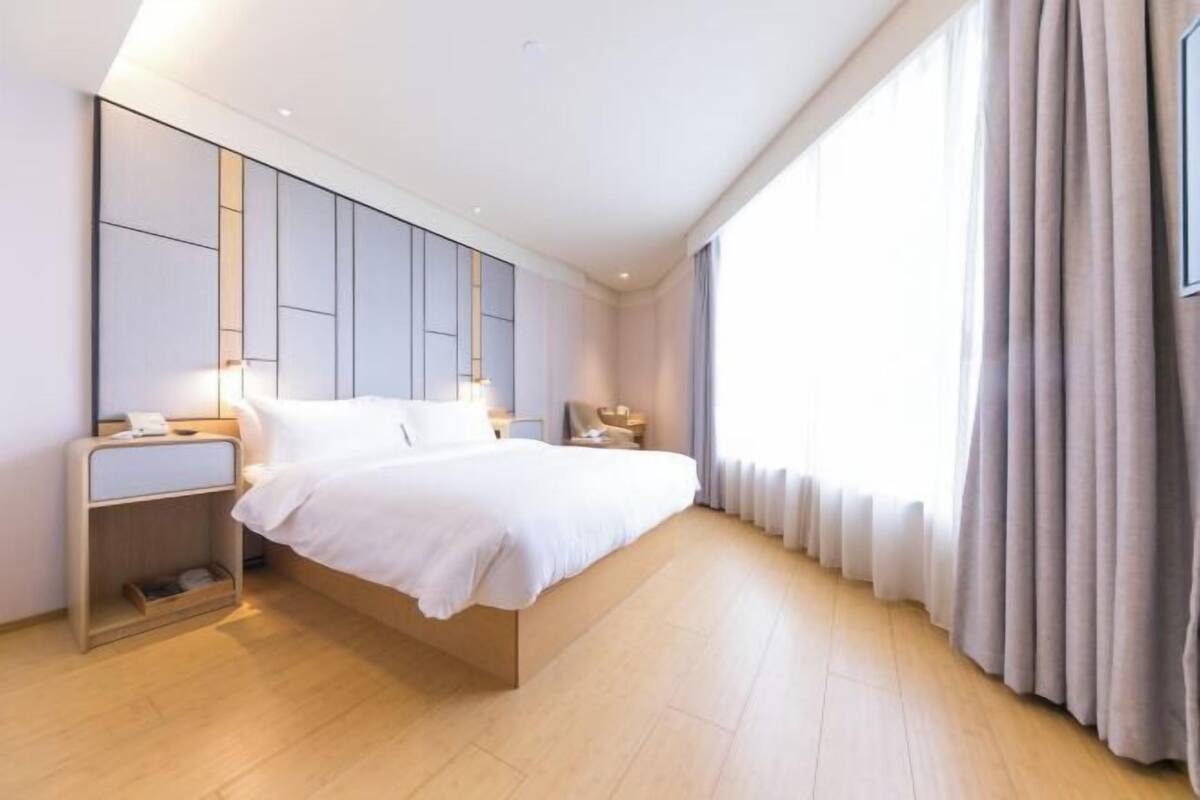 Una habitación de hotel moderna con una cama grande, mesitas de noche y un amplio ventanal con cortinas.