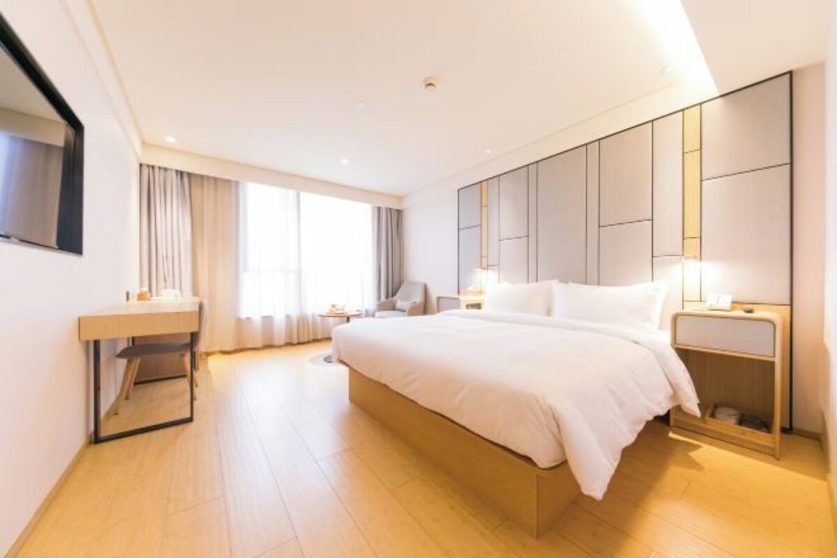 A modern hotel room with a large bed, a bedside table, a mirror, a desk, and a chair.