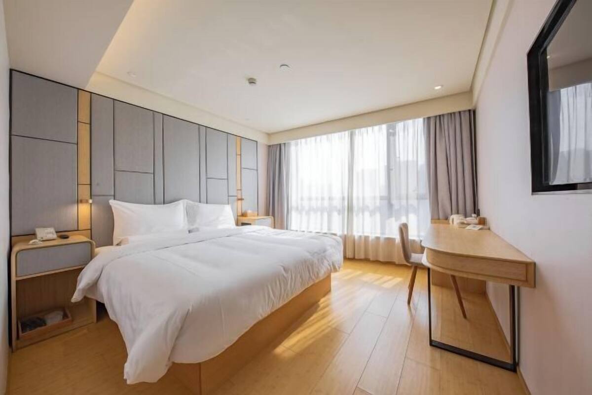 Habitación de hotel moderna con una cama grande, mesitas de noche, un escritorio y una ventana con cortinas.