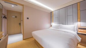 Une chambre d’hôtel moderne avec un grand lit, une table de chevet en bois et une commode, ainsi qu’une porte donnant sur une autre pièce.