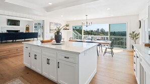 Una cocina amplia con una isla grande, armarios blancos y vistas al exterior.