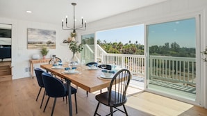 Comedor con mesa de madera dispuesta para cuatro, una araña y vistas a una piscina y paisaje a través de puertas correderas amplias.