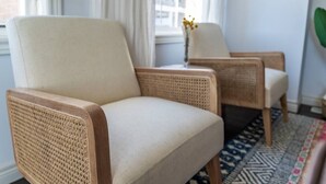 A room with two wicker chairs, a patterned rug, and a vase with yellow flowers on a table. - ✦Boho-Chic Home: 4 BR + ❤ of City + Patio & BBQ (Kitchener)