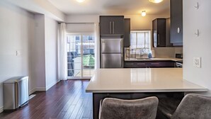 A modern kitchen with a central island, stainless steel appliances, and a sliding glass door leading to a balcony. - ✦Boho-Chic Home: 4 BR + ❤ of City + Patio & BBQ (Kitchener)