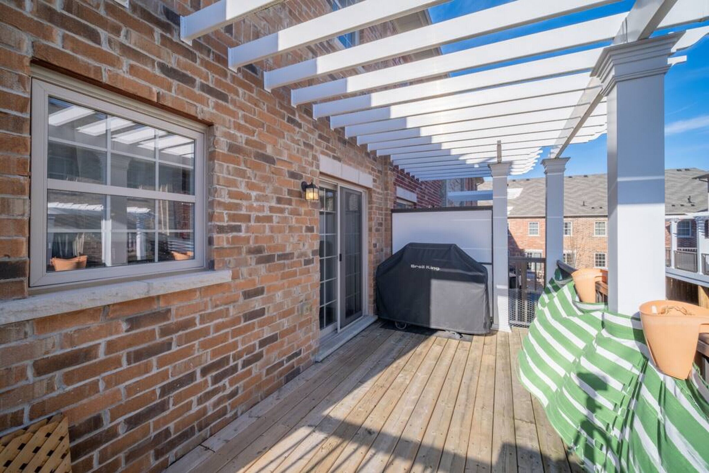 A brick exterior wall, a window, a sliding glass door, a grill, a wooden deck, and a pergola.