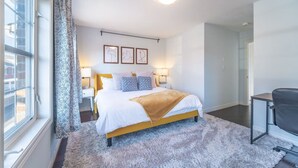 A bedroom with a bed, bedside tables, a desk, a chair, a window with curtains, and wall art. - ✦Boho-Chic Home: 4 BR + ❤ of City + Patio & BBQ (Kitchener)