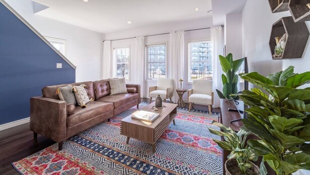 A living room with a brown leather sofa, a coffee table, and patterned rugs. - ✦Boho-Chic Home: 4 BR + ❤ of City + Patio & BBQ (Kitchener)