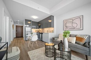 A modern living room with a grey sofa, a coffee table, and a dining area with a white table and chairs. - Modern Suite with City Views (Kitchener)