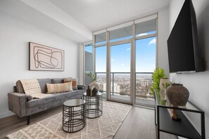 Un soggiorno moderno con un divano grigio, un tavolino, una TV e una grande finestra con vista sulla città.