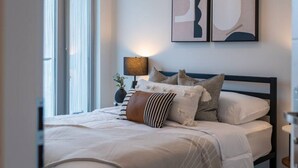 Una cama bien hecha con varios almohadones y una lámpara de noche.
