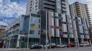 Un edificio moderno y alto, con fachada de vidrio, situado en la intersección de una calle con automóviles y semáforos.