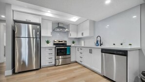 A modern kitchen with stainless steel appliances, white cabinetry, and a wooden floor. - Bright & Cozy 1BR Basement Unit (Kitchener)
