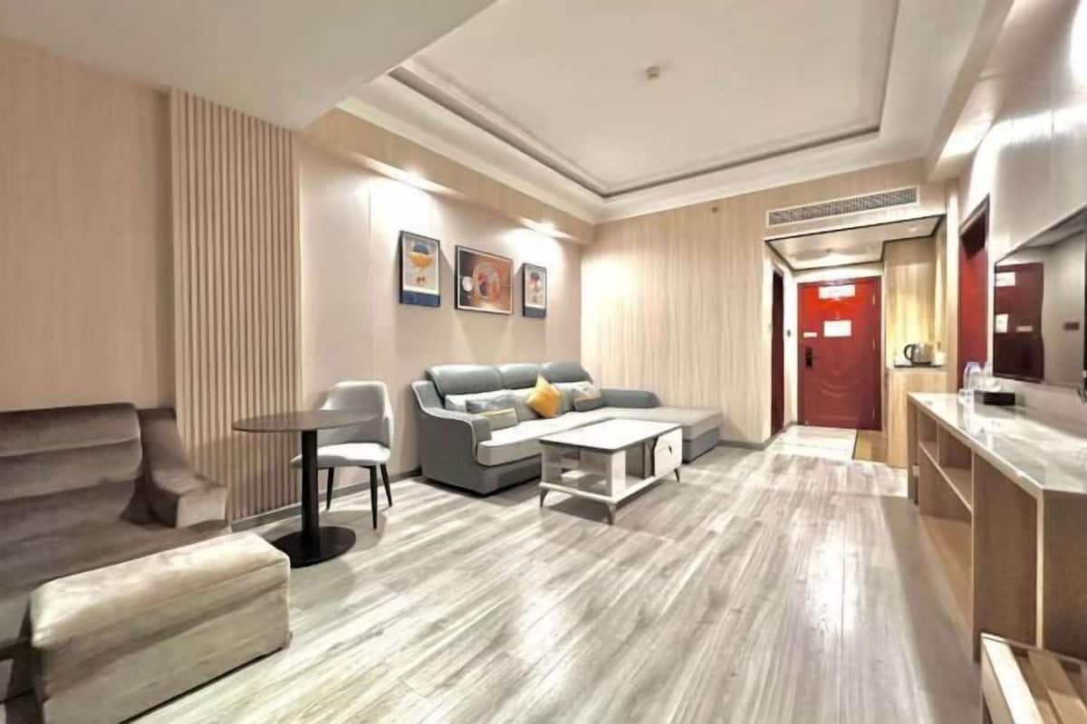 A modern living room with a grey sofa, a small round table, and a coffee table. There is a red door in the background and a wooden cabinet to the right.
