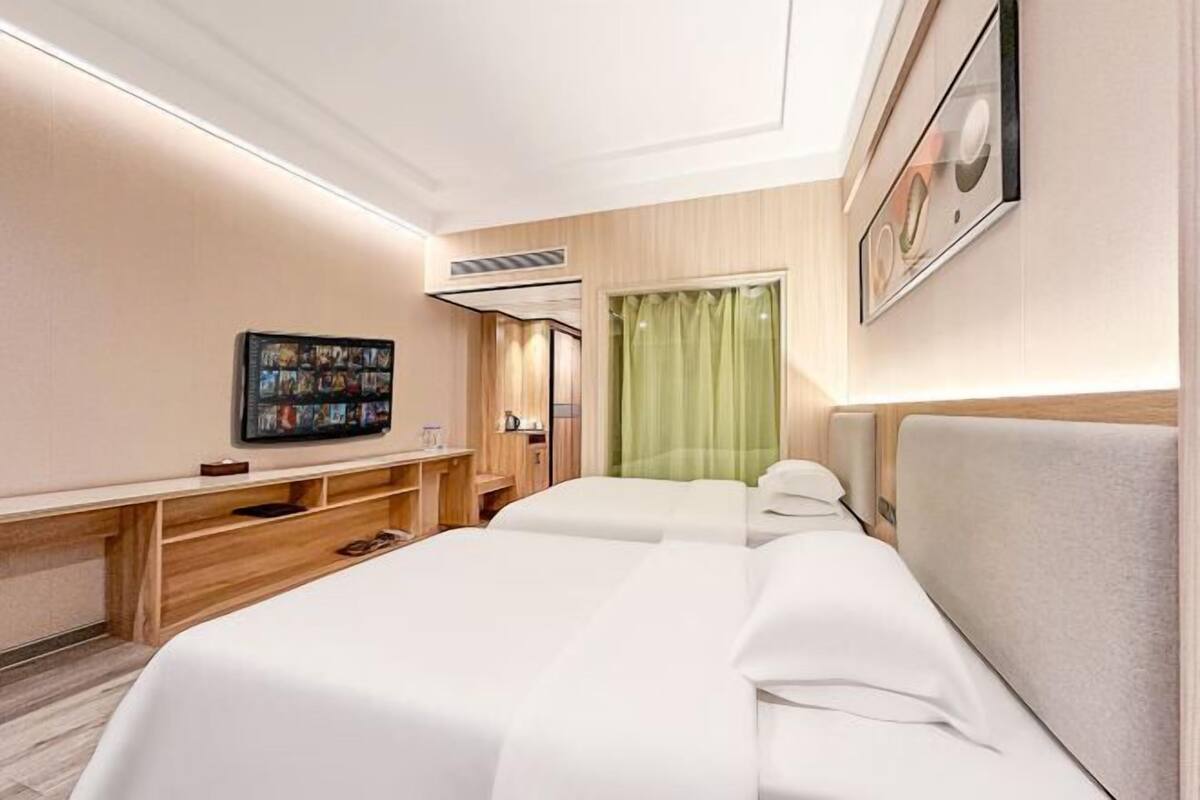Une chambre d’hôtel avec deux lits, un téléviseur à écran plat, un bureau en bois et un rideau vert.