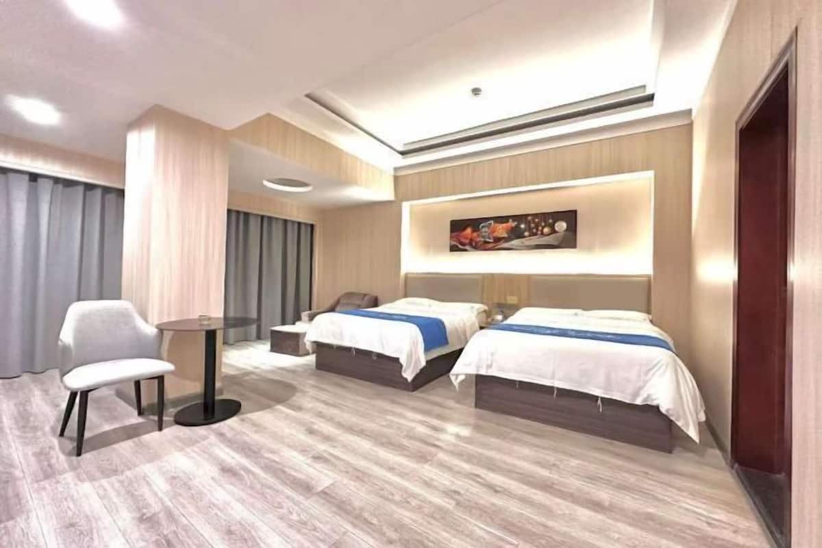 A modern hotel room with two beds, a small table, and a chair.