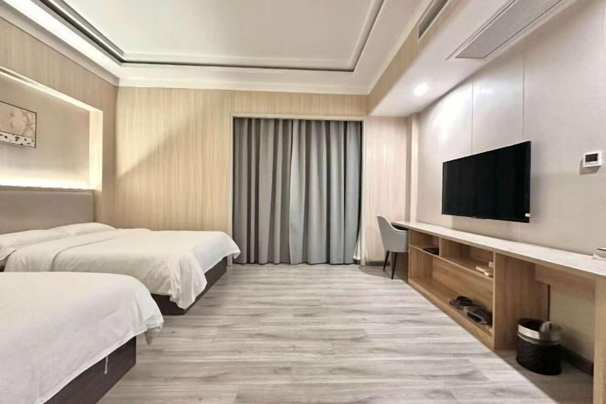 Une chambre d’hôtel avec deux lits, une télévision, un bureau et une grande fenêtre avec des rideaux.