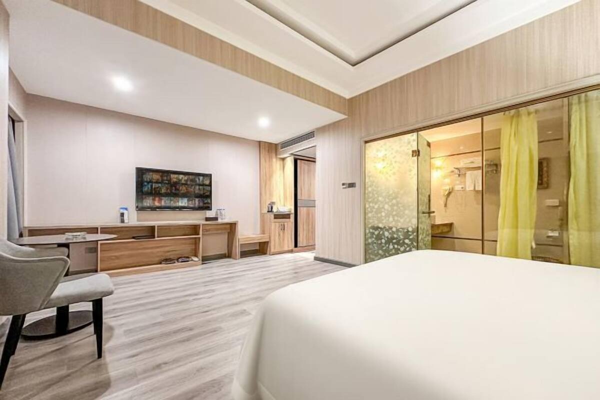A modern bedroom with a large bed, a desk with a chair, a small table, and a large window with curtains.