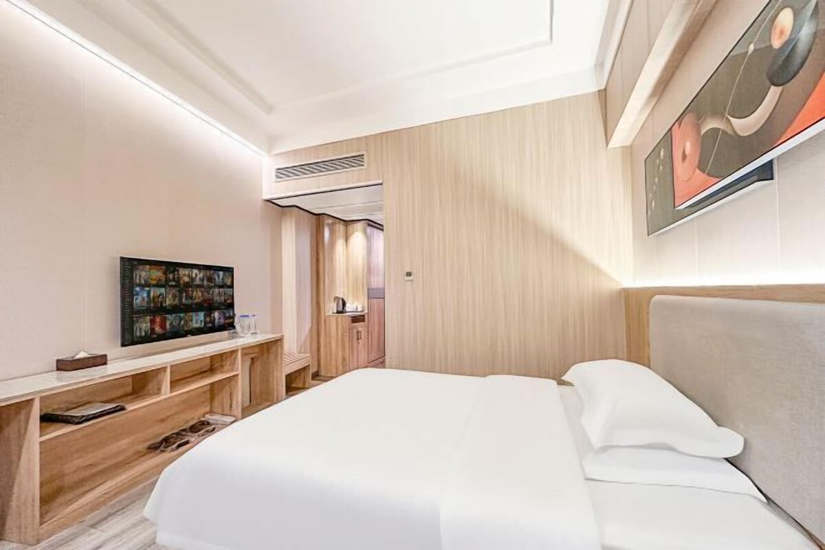 A modern hotel room with a large bed, a TV on a wooden console, and a painting on the wall.