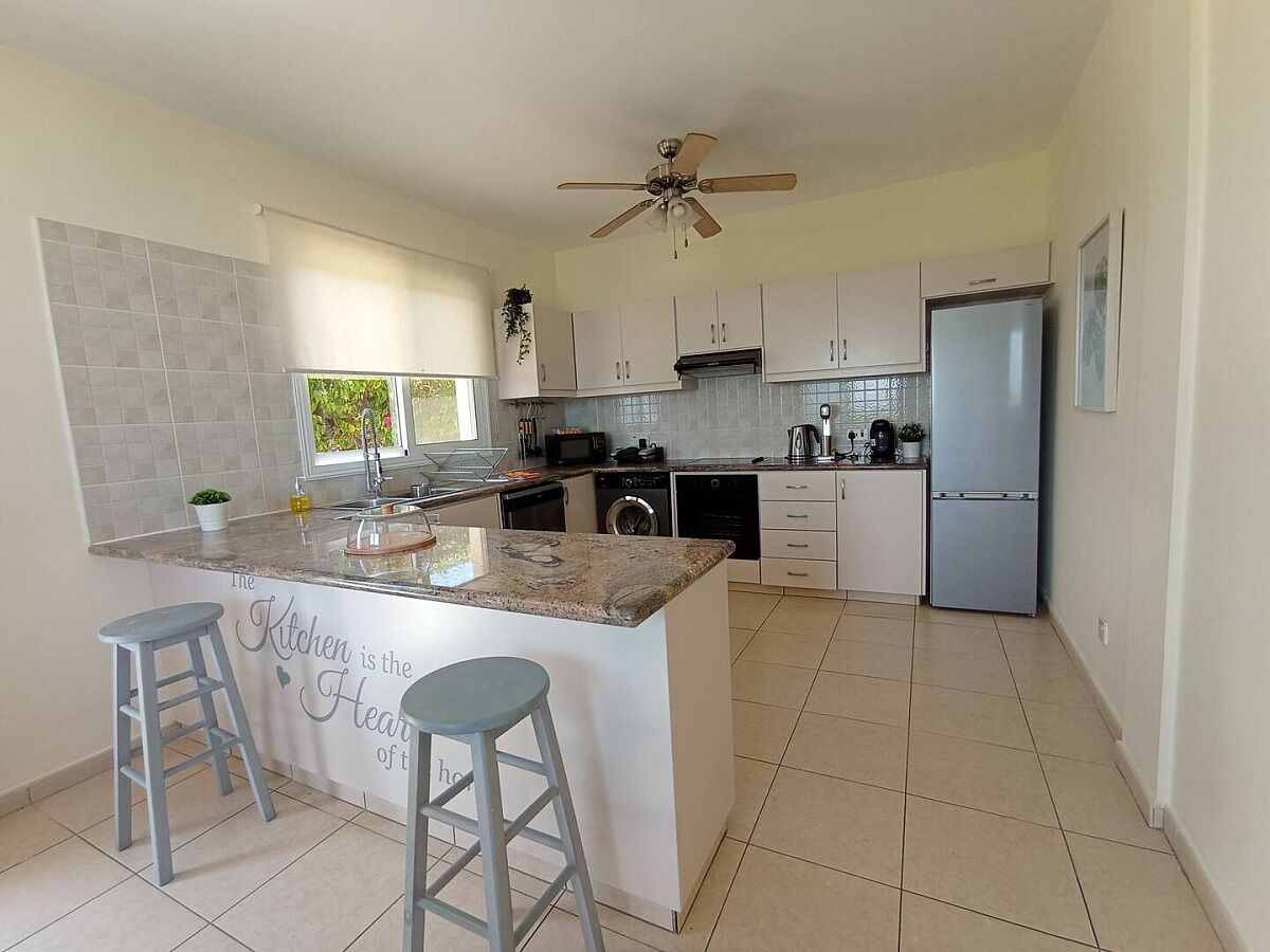 A modern kitchen with a central island, bar stools, a ceiling fan, and a refrigerator.