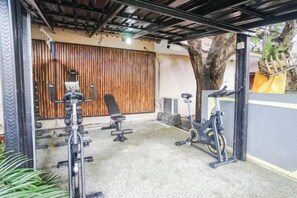 Zona de gimnasio al aire libre con equipamiento de ejercicio, incluyendo un banco, una bicicleta estática y una máquina de remo.