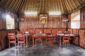 Un restaurante con paredes de madera y techo de paja. Mesas y sillas dispuestas para comer.